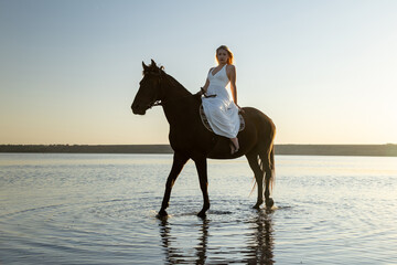 A woman in a white dress rides her horse through the shallow waters of Kuyalnik Lake at sunset, radiating grace and tranquility.