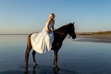 A woman in a long white dress sits elegantly on her horse by Kuyalnik Lake, embraced by the calm of sunset.