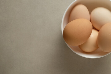 Fresh eggs in a white bowl on a neutral surface in natural light