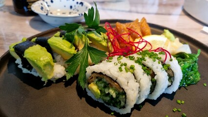 Sushi rolls with rice and toppings on a black plate on a table with a bowl of soy sauce. Proper nutrition.