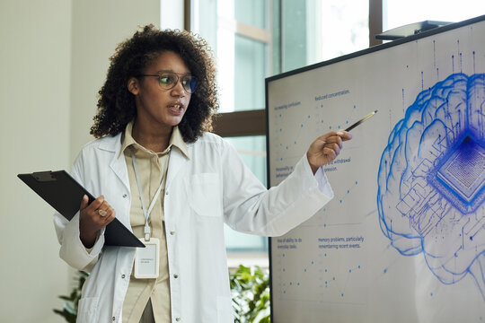Black female scientist or doctor presenting scientific data on digital screen showing brain diagram with microchip, holding clipboard and pen, standing at medical conference or in laboratory - Powered by Adobe
