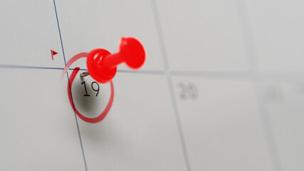 Red pushpin marking the 19th on a calendar with red circle, symbolizing appointment or scheduled event