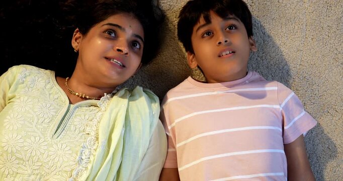 Indian mother son talking while lying on carpet in modern home, spending quality play time together, sharing affection, love, joy, warmth, bonding, parent child relationship, family lifestyle indoors