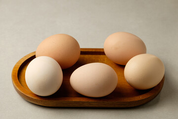 A simple wooden tray displays five eggs in various shades of brown and white