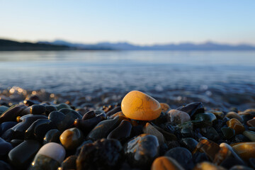 Close up of a single orange pebble on a rocky beach with the ocean and mountains in the background