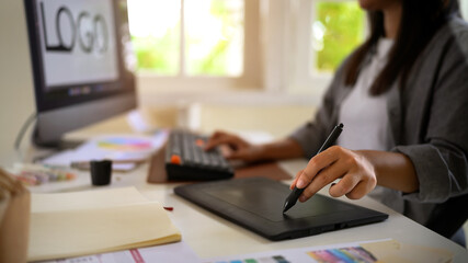 Female designer developing logo concept using pen tablet and desktop monitor in a cozy home office