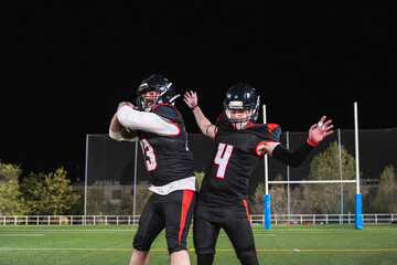 Two american football players interacting on a stadium field at night, focusing on teamwork and competitive sport