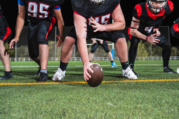 American football players in uniform lining up on the green turf, hands on knees, ready for the kickoff or start of play