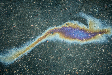 Polluting oil stain on dark asphalt creating iridescent rainbow colors, showing environmental issue.