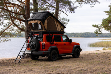 A car with a tent on the roof on the sandy shore of the lake