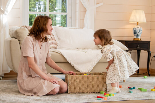 Mother and little girl playing with colorful wooden building blocks
