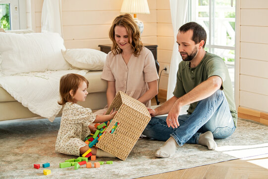Parents and little girl playing with colorful wooden building blocks