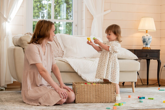 Mother and little girl playing with colorful wooden building blocks