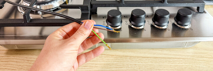 Hand tinkering colorful wires near stove knobs, embodying curious engineering spirit, possibly DIY Day or Inventor's Month April 5 2025, Barcelona, Spain