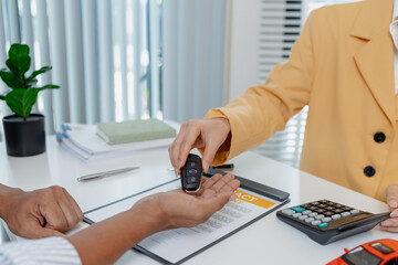 A businesswoman in a yellow suit is consulting with a male client about car purchase contracts, showing documents and car models on the desk to finalize agreement and transaction.