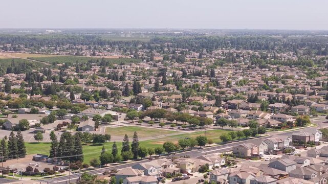 Lateral drone shot moving over Ripon, California, showing residential houses, road lined with trees, and surrounding fields.