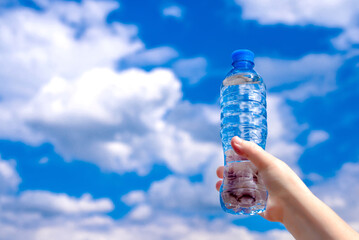 A girl holds a bottle of drinking water in her hand against a blue sky background