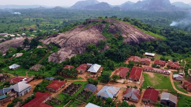 Aerial view of a monolithic rock formation rising dramatically above the lush green landscape and small village, Akure, Ondo, Nigeria.