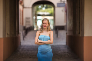 Young woman, blonde, blue eyes, slim, wearing a light blue dress, looking freely and independently at camera, with her arms crossed, representing the new generations. Concept: femininity, youth.
