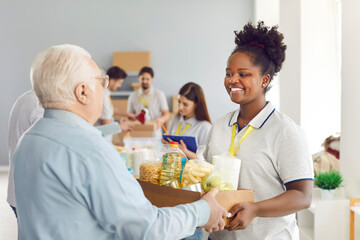 Close-up of an African American female volunteer giving a box of food to an older man. A group of people participate in humanitarian aid. Help for the elderly. Concept donation bag, food bank