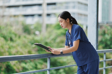 Young doctor reading medical records on clipboard in hospital balcony