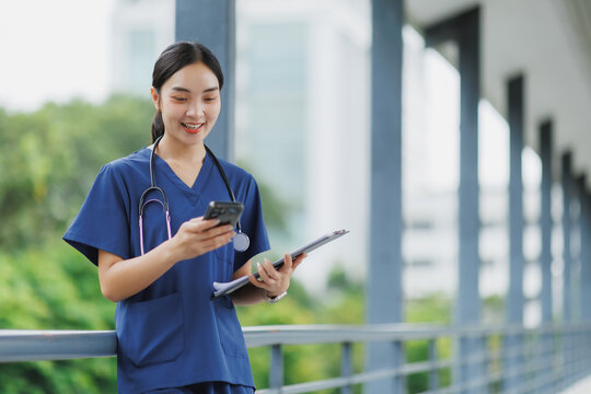 Smiling doctor using mobile phone and holding medical record in hospital corridor