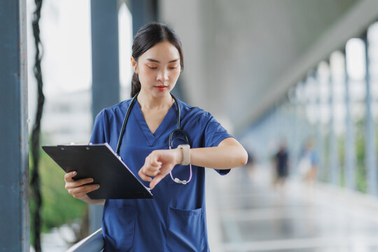 Nurse checking time and holding clipboard in hospital corridor