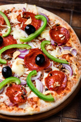 Pizza with chorizo ​​sausage, mozzarella cheese, green pepper and black olives. Rustic wooden background. Soft focus.	