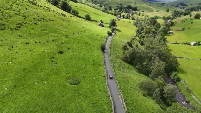 Aerial view of a winding road slicing through lush green hills and vibrant trees, creating a beautiful contrast of colors and textures, Hawes, England, United Kingdom.