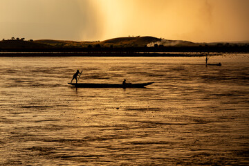 Traditional dugout canoe with silhouetted figures paddles across the wide Mahajilo River in Madagascar at golden sunset