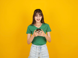 Woman using mobile phone, portrait of young caucasian pretty cute happy smiling positive 20s woman using mobile phone isolated on yellow studio background, copy space. Hold use mobile app idea.