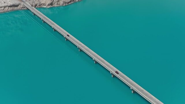 Aerial view of cars driving over a long bridge cutting through the turquoise waters of Baisha Lake contrasting with the tan mountains, Baisha Lake, China.