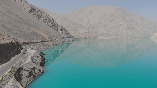 Aerial view of turquoise Baisha lake reflecting the mountains, with cars on the adjacent road, creating a stunning contrast, Baisha Lake, China.