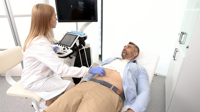 Ultrasound specialist doing ultrasonography of abdominal cavity for male patient with ultrasound machine at hospital