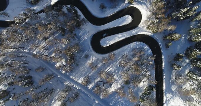 Aerial view of the winding Maloja Pass road cutting through a snow-blanketed landscape of trees, a striking contrast of dark asphalt and pristine white, Maloja Pass, Grisons, Switzerland.
