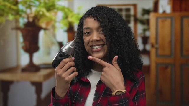 Woman in red plaid shirt points finger to electric drill in studio; diy empowerment confidence creativity.