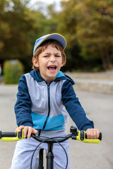 Obraz premium Happy Young Boy in a Cap and Hoodie Riding a Bicycle Outdoors and Smiling at Camera