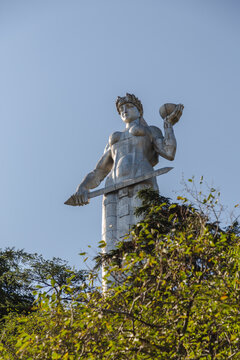 View of the imposing Kartlis Deda statue, a monumental figure holding a sword and a bowl, framed by lush greenery against a clear blue sky, Mother of Georgia, Tbilisi, Georgia.