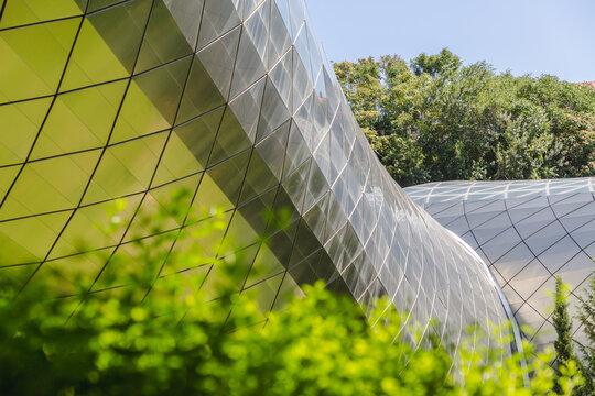 View of a modern architectural marvel with glass and metal facade curves gracefully against a backdrop of vibrant green trees, Tbilisi, Tbilisi, Georgia.