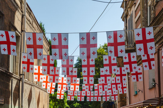 View of Georgian flags strung between aged buildings under a clear sky, creating a vibrant display of red and white, Tbilisi, Tbilisi, Georgia.