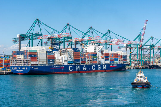 Cargo ship owned by "CMA CGM" at a container terminal with numerous stacked shipping containers of varying colors on its deck. 