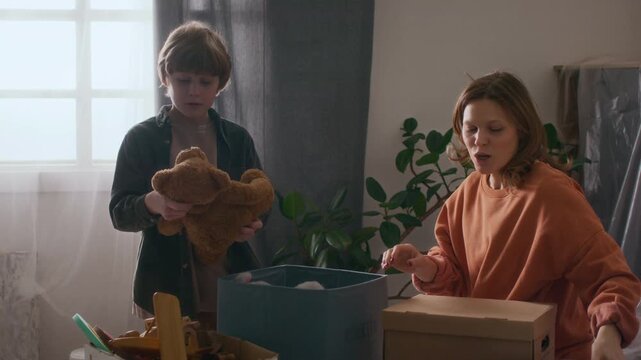 Mother and her son unpacking different stuffed toys from boxes after just moving into new apartment