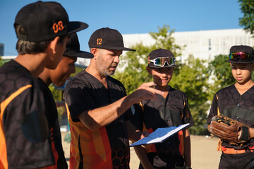 Coach explaining game strategy on a clipboard to his youth baseball team during practice