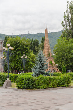 View of a striking Eiffel Tower replica amidst lush green trees and manicured hedges under a cloudy sky, Goris, Syunik Province, Armenia.