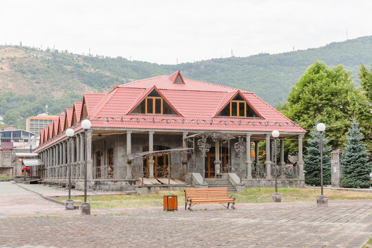 View of a grand, stone building with a striking red roof, standing proudly against a backdrop of verdant mountains, evoking a sense of timeless elegance, Goris, Syunik Province, Armenia.