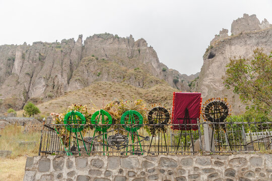 View of vibrant green wreaths and a striking red cloth stand in solemn contrast against the ancient, weathered stone mountains, Goris, Syunik Province, Armenia.