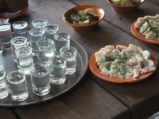Traditional Slavic table setting with vodka shots, salted lard with herbs, and pickles served on rustic wooden surface