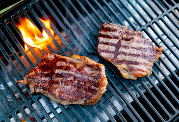 Steaks grilling over an open flame at a backyard barbecue event during a sunny afternoon