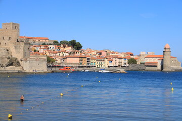 View across bay of Collioure old town, France featuring man wading in water with Notre-Dame-des-Anges church visible 