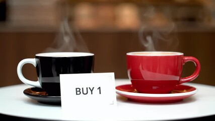 Steaming black and red coffee cups with a 'Buy 1' offer card on a cafe table, hot beverages for promotion